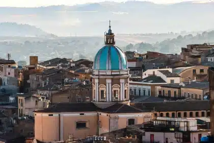 Vista distante di un campanile in marmo avvolto da ponteggio metallico con operai in silhouette