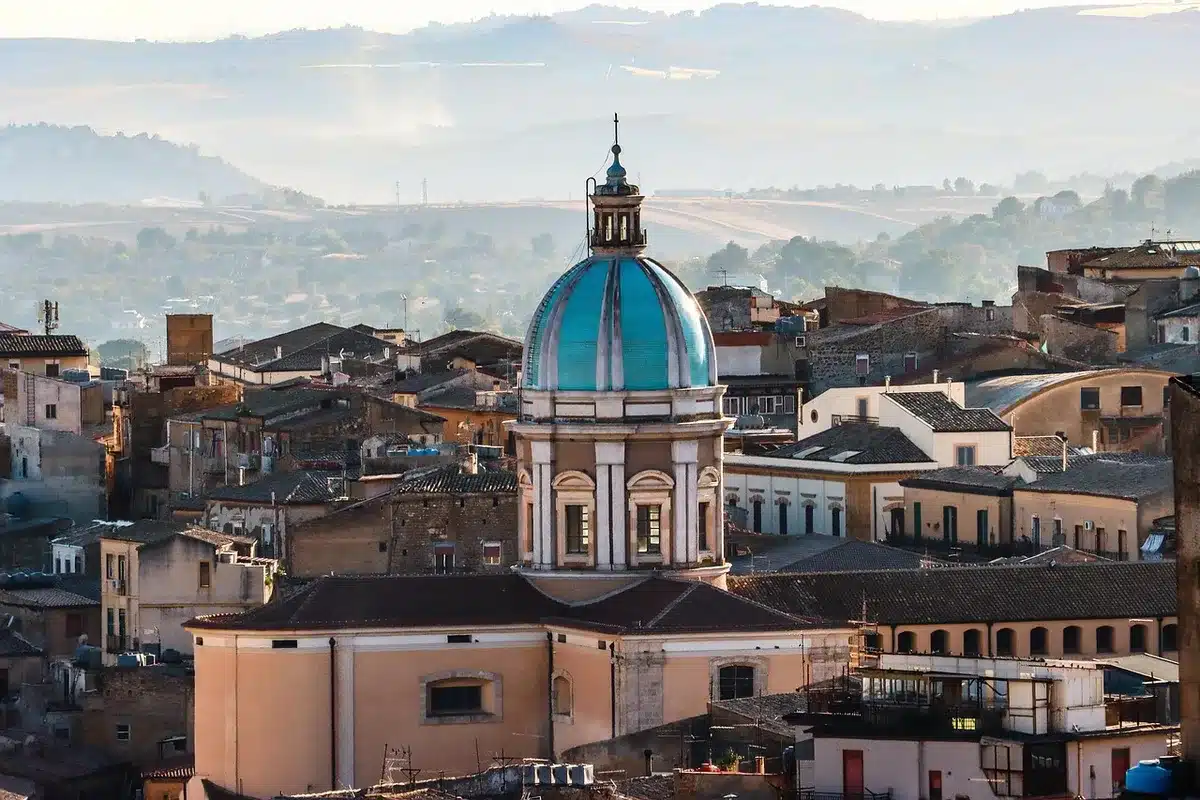 Vista distante di un campanile in marmo avvolto da ponteggio metallico con operai in silhouette