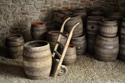 Magazzino di invecchiamento con file di botti e mani anonime che controllano una botte
